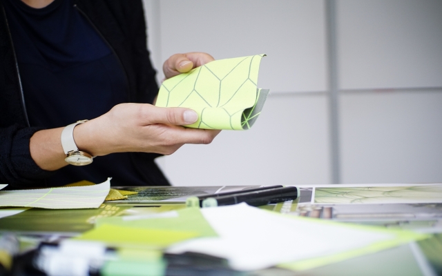 Woman-holds-green-yellow-material-in-the-background-is-a-table-with-similar-materials-to-see