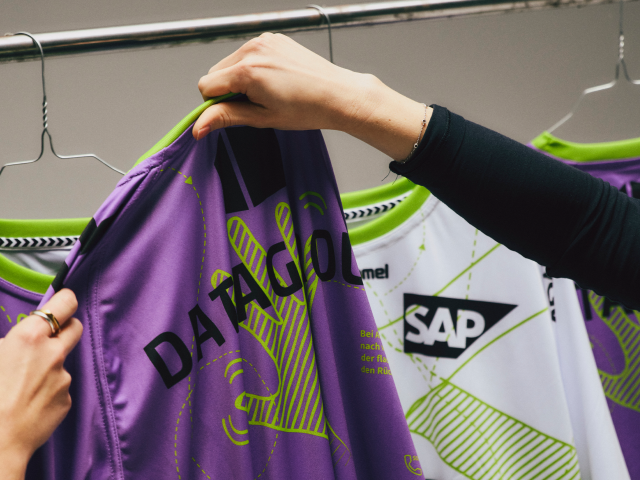 two-women-holding-purple-sustainabilityjersey-from-tvb-stuttgart-backgrownd-more-jerseys-visible