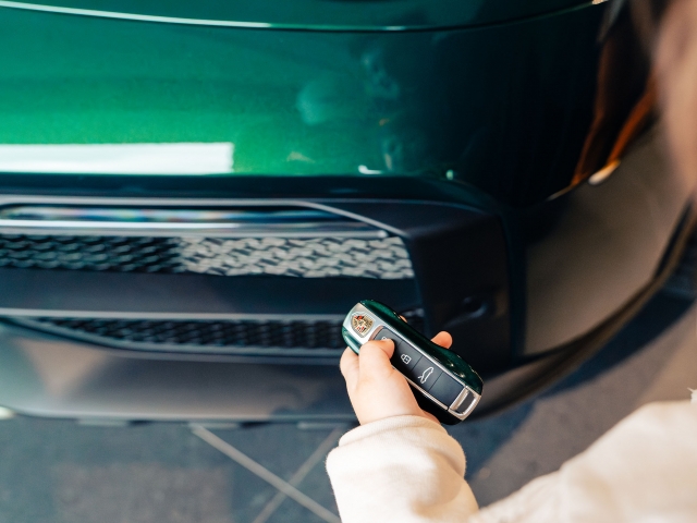 child-presses-car-remote-control-porsche-dakar-dark-green-in-the-background