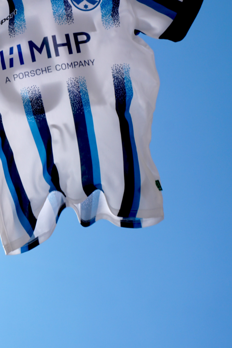 blue-white-striped-jersey-with-mhp-logo-and-stuttgarter-kickers-logo-flying-in-front-of-blue-sky